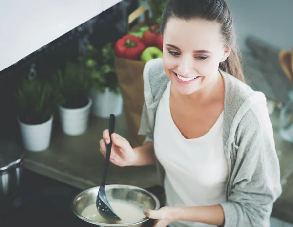 Eine junge Frau bereitet in der Küche Pfannkuchen zu, während sie am Tisch steht. Frau in der Küche. Kochen in der Küche. — Stockfoto
