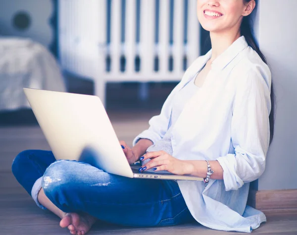 Young woman sitting on the floor near childrens cot with laptop. Young mom — Stock Photo, Image