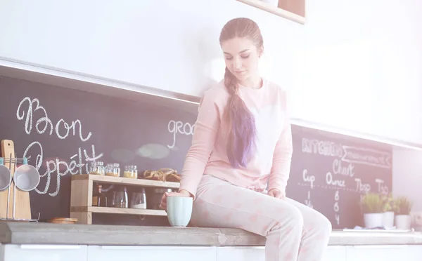 Junge Frau sitzt auf Tisch in der Küche. — Stockfoto