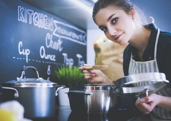 Young woman standing by the stove in the kitchen . — Stock Photo, Image