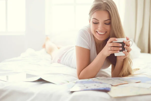 Relaxado jovem mulher sentada na cama com uma xícara de café e tablet digital — Fotografia de Stock