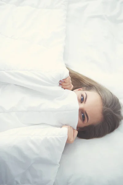 Cara primer plano de una hermosa mujer joven escondiendo su cara debajo de la sábana —  Fotos de Stock