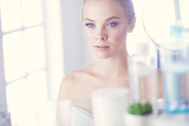 Bornozlu genç kadın banyo aynasına bakıyor.