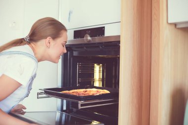 Mutlu genç bayan evde pizza pişiriyor.