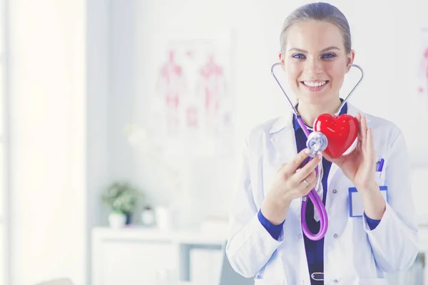 Un médico con estetoscopio examinando el corazón rojo, aislado sobre fondo blanco — Foto de Stock