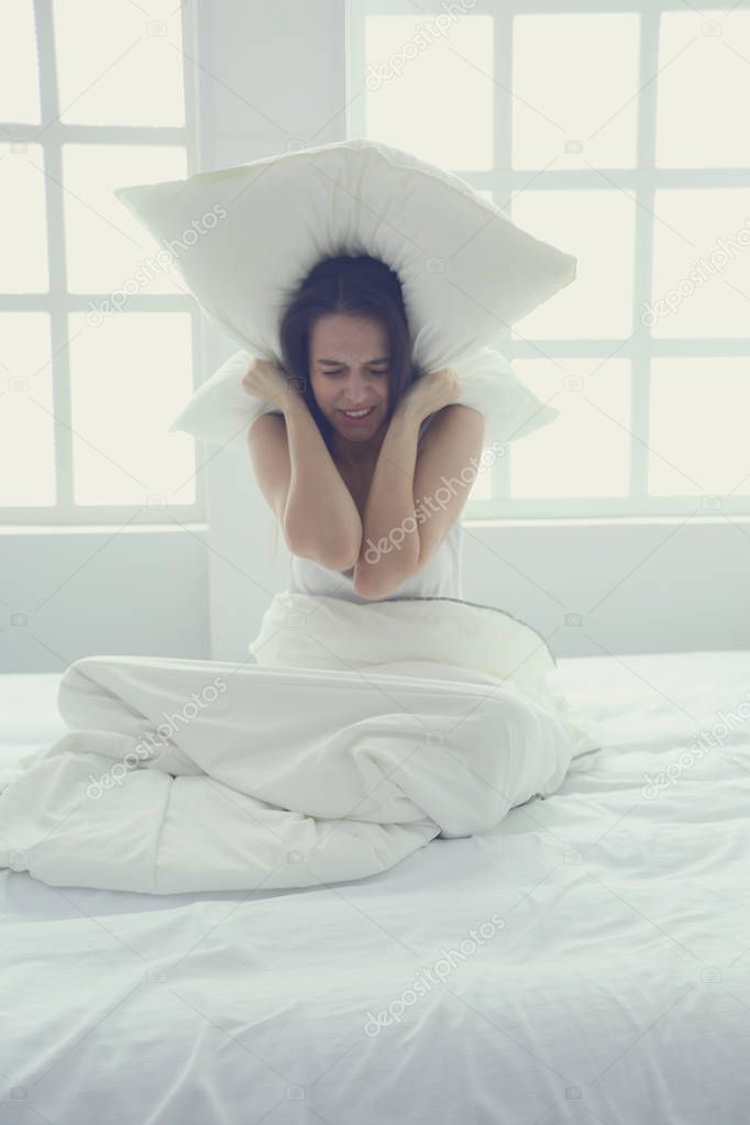 Young caucasian woman covering her head and ears with pillows.