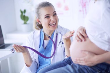 Steteskoplu genç bayan doktor hastanede hamile bir kadınla konuşuyor..
