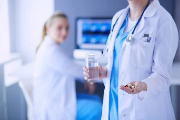 Aufnahme eines Arztes mit Tabletten und Glas Wasser in der Klinik mit einem Kollegen im Hintergrund. — Stockfoto