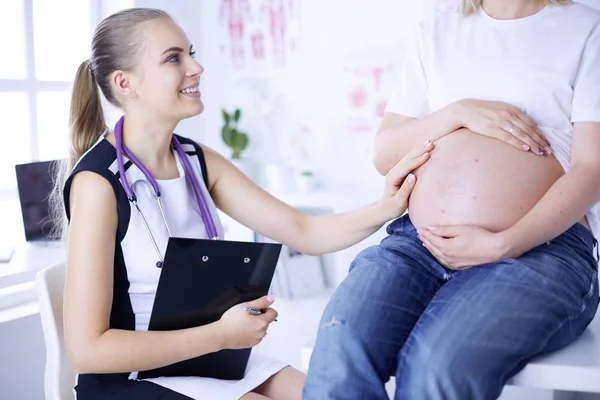 Mladá žena lékař vyšetřuje těhotnou ženu na klinice. — Stock fotografie