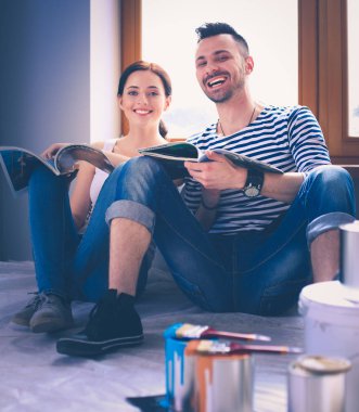 Yeni evin içini boyayan mutlu, gülümseyen genç bir çift portresi. Genç çift