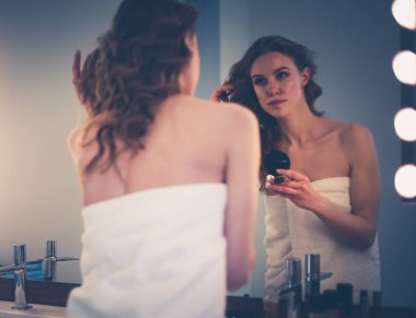 Genç bir kadın aynaya bakıyor ve makyaj yapıyor..