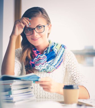 Kitapların arasında bir masada oturan genç bir kadın. Öğrenci