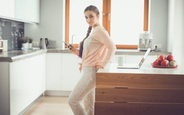 Cep telefonu ayakta modern mutfak kullanan kadın.