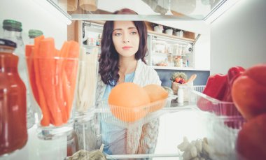 Sağlıklı yiyecek, sebze ve meyvelerle dolu açık buzdolabının yanında duran kadın portresi. Kadın portresi