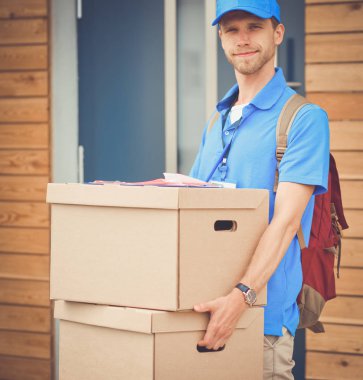 Mavi üniformalı gülümseyen kurye servis konseptine paket kutusu teslim eden teslimatçı. Mavi üniformalı gülümseyen teslimatçı.