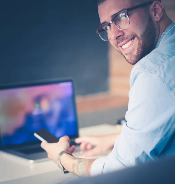 Ung man använder telefonen och fungerar på den bärbara datorn. — Stockfoto