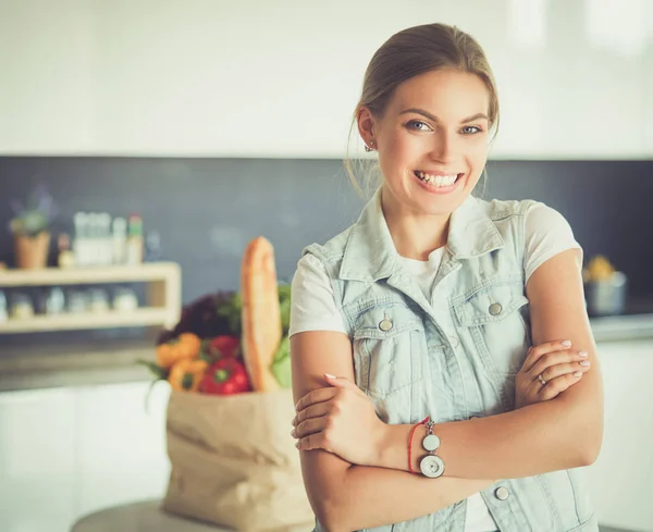 Jeune femme tenant sac d'épicerie avec des légumes. Debout dans la cuisine — Photo