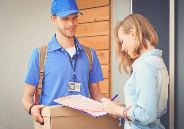 Repartidor sonriente con uniforme azul que entrega la caja de paquetes al destinatario: concepto de servicio de mensajería. Repartidor sonriente en uniforme azul — Foto de Stock