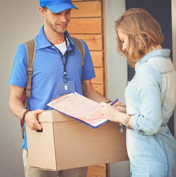 Mavi üniformalı gülümseyen kurye servis konseptine paket kutusu teslim eden teslimatçı. Mavi üniformalı gülümseyen teslimatçı.