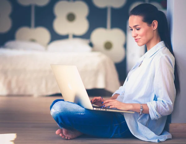 Ung kvinna som sitter på golvet nära barnens babysäng med laptop. Ung mamma — Stockfoto