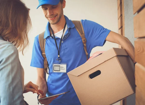 Mavi üniformalı gülümseyen kurye servis konseptine paket kutusu teslim eden teslimatçı. Mavi üniformalı gülümseyen teslimatçı.