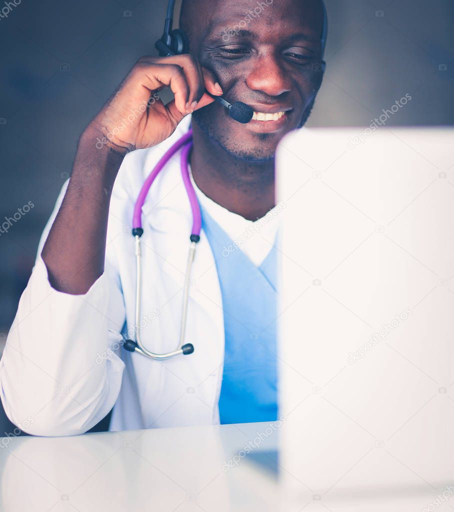 Portrait of young male doctor wearing headset while using computer at desk in clinic. Doctor.