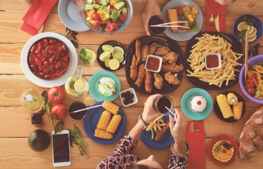 Ahşap masada otururken birlikte yemek yiyen bir grup insanın üst düzey görüntüsü. Masada yemek var. İnsanlar fast food yiyor..