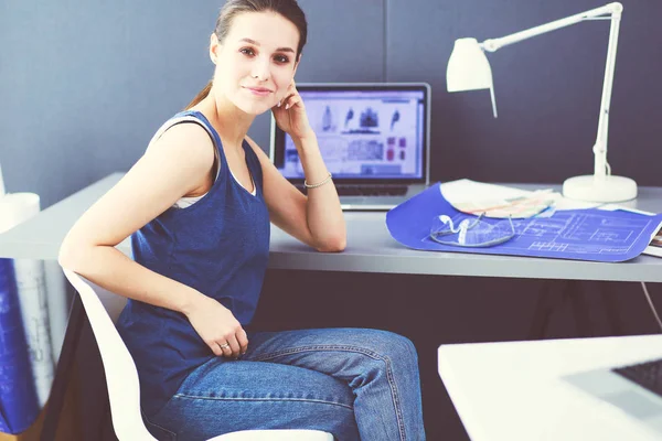 Jonge vrouw zit aan het bureau met instrumenten, plan en laptop. — Stockfoto