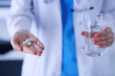 Doktorlar ellerinde haplar ve klinikte bir bardak su tutarken..