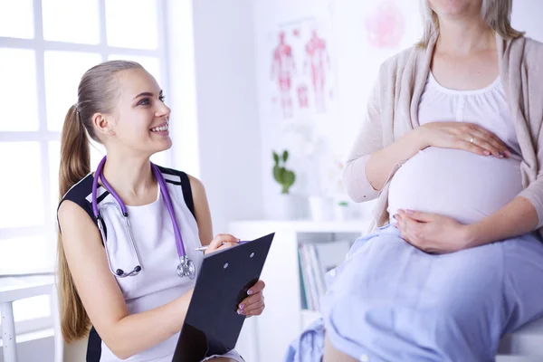 Ung kvinna läkare med stetoskop och tablett talar med gravid kvinna på sjukhus. — Stockfoto