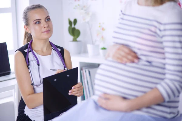 stock image Young woman doctor with stethoscope and tablet speaking with pregnant woman at hospital.