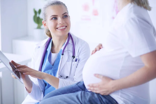 Usmívající se žena lékař ukazuje obrázky na tabletu těhotné mladé ženě v nemocnici. — Stock fotografie