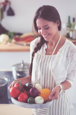 Mutfakta elinde sebzelerle gülümseyen genç bir kadın. Gülümseyen genç kadın