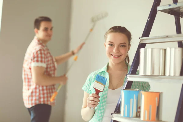 Retrato feliz sonriente joven pareja pintando la pared interior de la casa nueva. Pareja joven — Foto de Stock