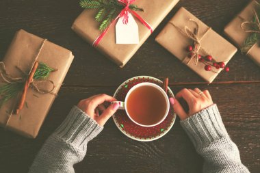 Noel hediye kutusu ile masaya oturan kadın. Kadının elleri