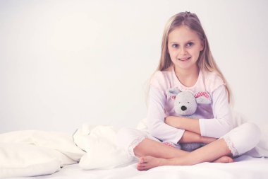 Küçük kız yatak odasında yatağın üzerine oturuyor. Küçük kız yatakta oturuyor ve bir pijama giymiş .
