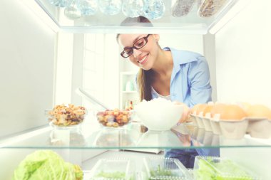 Sağlıklı yiyecek, sebze ve meyvelerle dolu açık buzdolabının yanında duran kadın portresi..