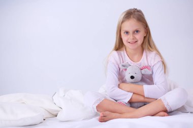 Küçük kız yatak odasında yatağın üzerine oturuyor. Küçük kız yatakta oturuyor ve bir pijama giymiş .