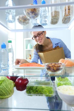 Sağlıklı yiyecek, sebze ve meyvelerle dolu açık buzdolabının yanında duran kadın portresi..