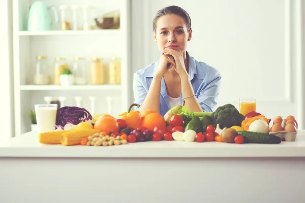 Mulher jovem e bonito sentado à mesa cheia de frutas e legumes no interior de madeira. — Fotografia de Stock