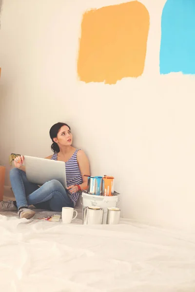 Retrato de mujer joven mientras pinta nuevo apartamento, sentado con el ordenador portátil. Mujer joven con portátil — Foto de Stock