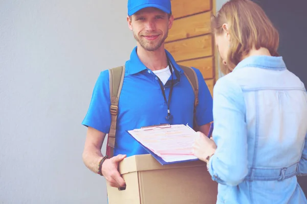 Repartidor sonriente con uniforme azul que entrega la caja de paquetes al destinatario: concepto de servicio de mensajería. Repartidor sonriente en uniforme azul — Foto de Stock