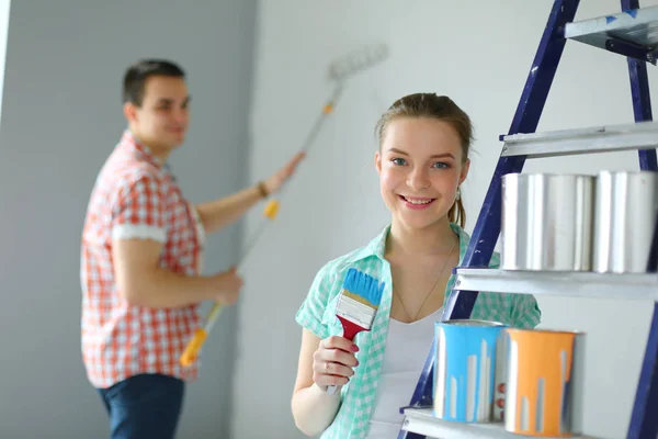 Портрет счастливой улыбающейся молодой пары, рисующей внутреннюю стену нового дома. Молодая пара — стоковое фото