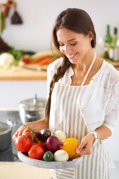 Улыбающаяся молодая женщина с овощами, стоящими на кухне. Улыбающаяся молодая женщина — стоковое фото