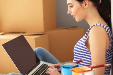 Yeni daire dizüstü bilgisayar ile oturup, boyama sırasında genç kadın portre. Dizüstü bilgisayar ile genç kadın