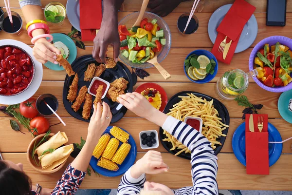 Vista superior do grupo de pessoas que jantam juntas enquanto estão sentadas à mesa de madeira. Comida na mesa. As pessoas comem fast food. — Fotografia de Stock