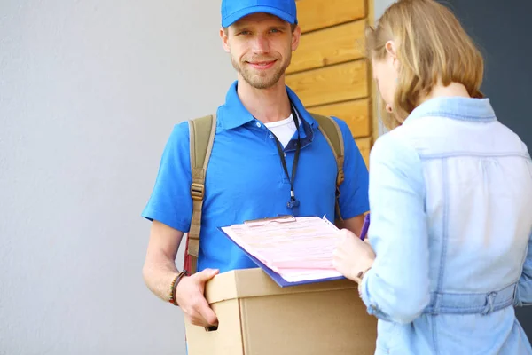 Repartidor sonriente con uniforme azul que entrega la caja de paquetes al destinatario: concepto de servicio de mensajería. Repartidor sonriente en uniforme azul — Foto de Stock