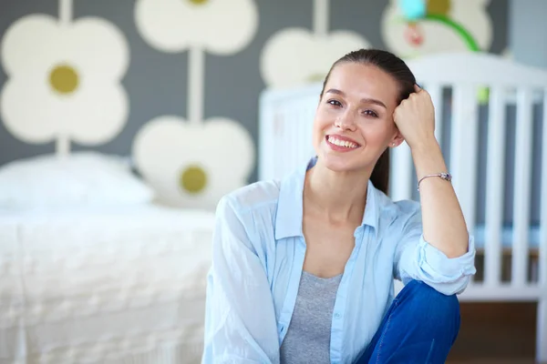 Giovane donna seduta sul pavimento vicino lettino per bambini. Giovane mamma . — Foto Stock