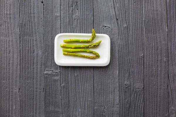 Fresh asparagus served on white plate on rustic wooden table background, top view. — Stock Photo, Image