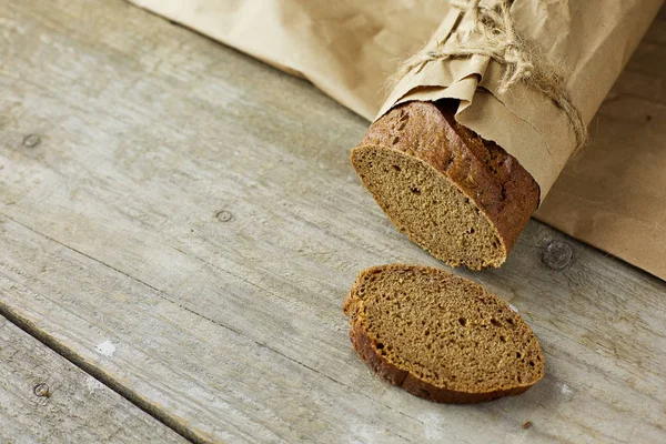 Skivad brödlimpa förpackad i papper på träbord. — Stockfoto